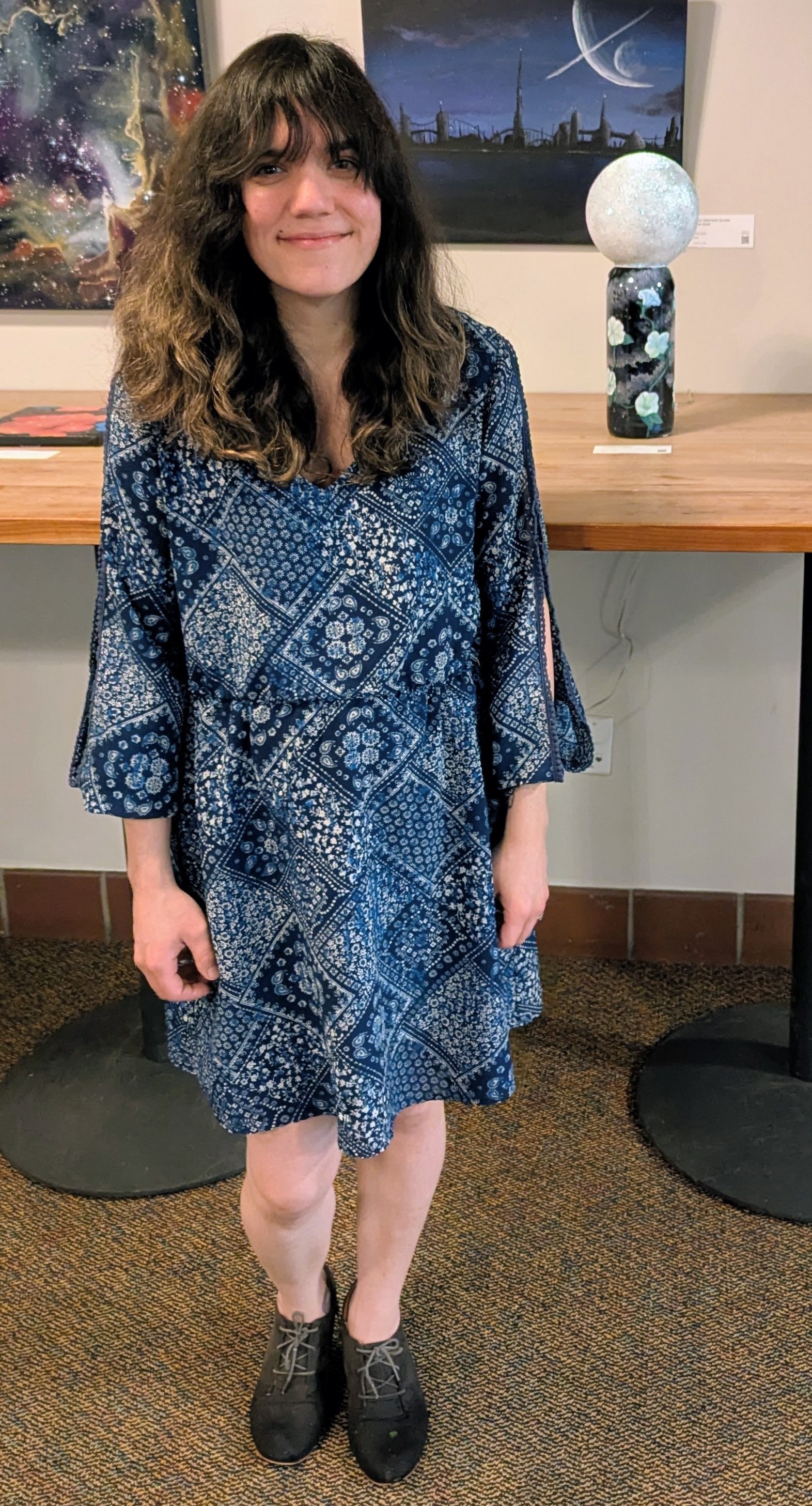Photograph of Heather Thomas, a brunette woman standing in front of a table holding her moonflower lamp piece